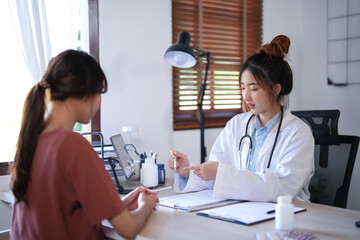 Asian psychologist women showing thermometer to explaining for reading temperature results about testing fever to patient while giving counseling mental health therapy to female patient in clinic