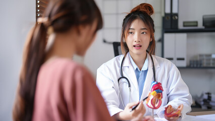 Asian cardiologist doctor women pointing on anatomical of human heart model to explaining medical...