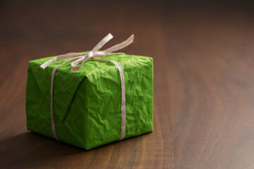 Green paper gift box with paper ribbon on walnut wood table with copy space