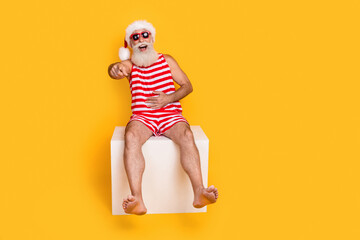 Full length photo of cool cheerful elderly guy wear new year swimsuit hat sunglass laughing pointing you empty space isolated yellow color background