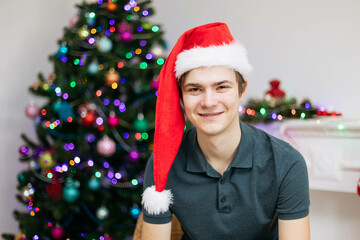 Young cute guy in santa hat looking at camera on christmas decoration background