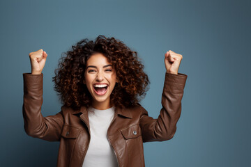 Happy curly  woman in white t-shirt raise hands up isolated on blue background. The concept of winning, good luck or winning - obrazy, fototapety, plakaty