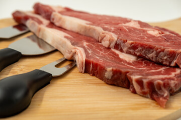 Raw ribeye on a wooden serving plate against a white background