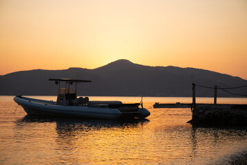 A majestic sunset over the mountains with a boat on the sea creates a picturesque scene of natural beauty.  Highlighting the mountains, sea, and a boat against the backdrop of the setting sun