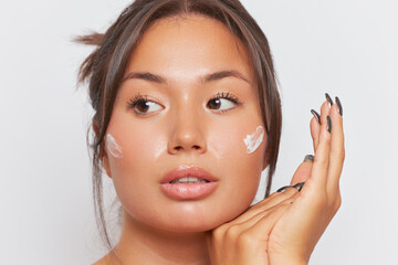 Portrait of Chinese girl with olive skin holding hands under her chin looking away, skincare...