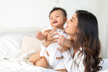 Obraz na płótnie Canvas Portrait of enjoy happy love family asian mother playing with adorable little asian baby, newborn, infant.Mom touching care with cute son in a white bedroom.Love of family concept