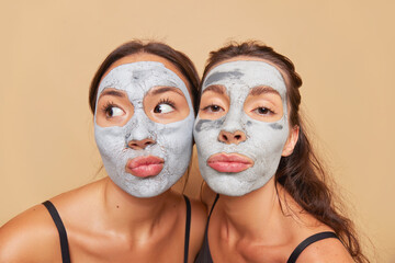 Close up of two girlfriends inside studio cheek to cheek, both doing clay cosmetic mask, skincare concept, copy space