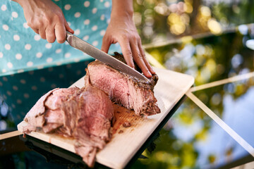 Housewife with a large knife cuts slices of juicy roast beef on a cutting board on a mirror table