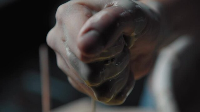 Potter squeezes a dirty sponge from clay into a basin with muddy water. Close-up, only hands in the frame. Tools for modeling clay in a pottery workshop.