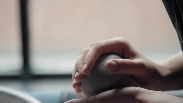 A ball of white clay in the hands of the potter. Preparation for modeling from clay: a woman holds a ball in hand and warms up. Close-up, natural light. Only hands in the frame.