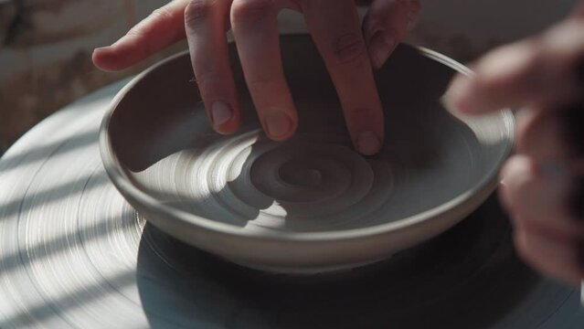 Potter makes a plate from white clay and draws a spiral inside, using a finger. Process: the ceramist makes a pattern inside the pottery of clay, making a spiral. Close-up, only hands in frame