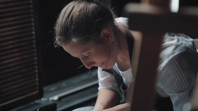 A potter woman works behind a potter's wheel, the look is directed downwards. She is in the workshop with the windows closed. Camera moves from person to product on a potter's wheel.