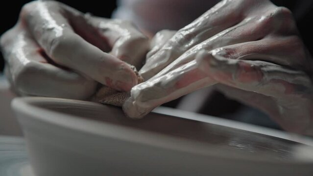 Clay plate on the potter's wheel, close-up. Potter with fingers and a sponge treats the edges of the clay product. Handicraft, pottery.