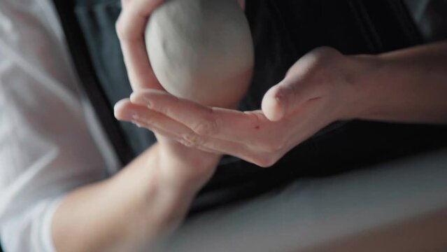 A woman kneads a piece of white clay in hands, warms it, rolls it and shifts it from palm to palm. Potter prepares the clay to work. Close-up, only hands.