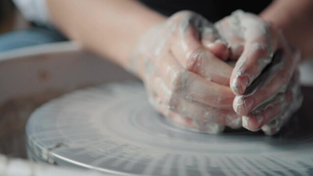 Dirty potter's hands in white clay making a ceramic product on a turning wheel, close up without face. Taken from a side