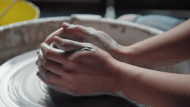 Potter's hands hold the clay on a rotating wheel, pottery. Close-up. Women's hands in clay.