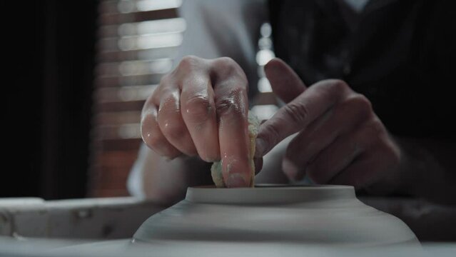 Hands of a potter and a clay jug. Potter holds a sponge on the neck hands in clay. Medium shot.