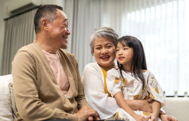 Portrait of happy love asian grandfather with grandmother and asian little cute girl enjoy relax at home.Young girl with their laughing grandparents smiling together.Family and togetherness