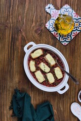 Fish baked in sour cream sauce with beans in tomato in a white ceramic form on a brown wooden background. Recipes: beans, fish.