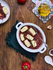 Fish baked in sour cream sauce with beans in tomato in a white ceramic form on a brown wooden background. Recipes: beans, fish.