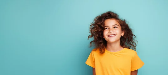Fotobehang Une jolie petite fille heureuse et souriante, arrière-plan coloré uni, image avec espace pour texte. © David Giraud