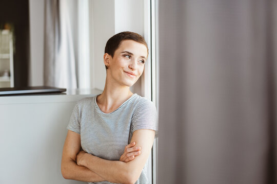 Smiling Young Woman Leaning on Wall and Looking Out Office Window