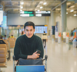 An Asian young  man wearing green color wool sweater and holding  airport cart at the  airport...