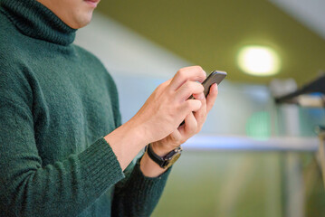 An Asian young  man wearing green color wool sweater and using smart phone at the  airport terminal  while waiting for boarding time, soft focus, travelling concept.