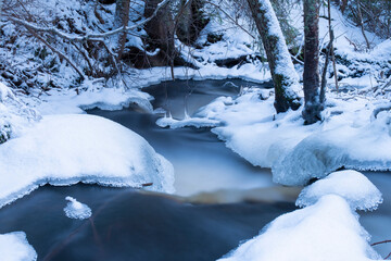 Blue hour by snowy and icy stream in the forest in Finland
