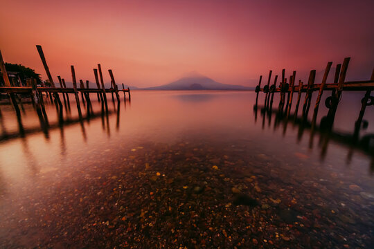 Fototapeta Wooden pier in Lake Atitlan at sunset with a Volcano in distance, Guatemalan Highlands, Solola Department, Guatemala