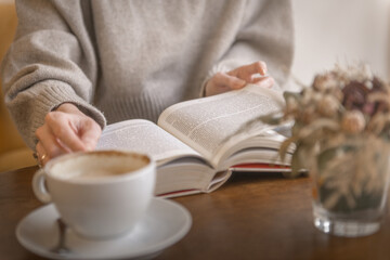 Young woman reading a book and drinking coffee in a cafe