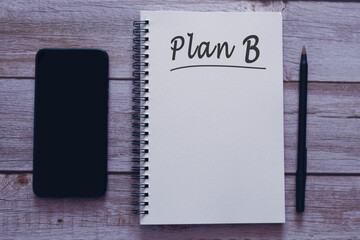 Plan B written on notepad with smartphone and pen on wooden desk.