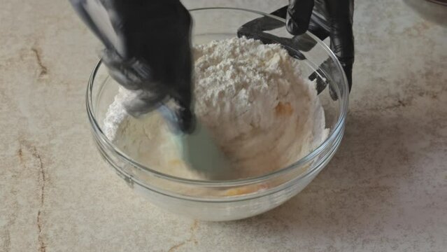 Mixing flour and eggs to obtain shortbread. A chef mixes flour with egg yolks in a glass bowl with a silicone spatula. Dynamic shooting