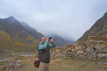 Fototapeta premium A male tourist takes pictures of a beautiful autumn mountain foggy landscape using a camera.