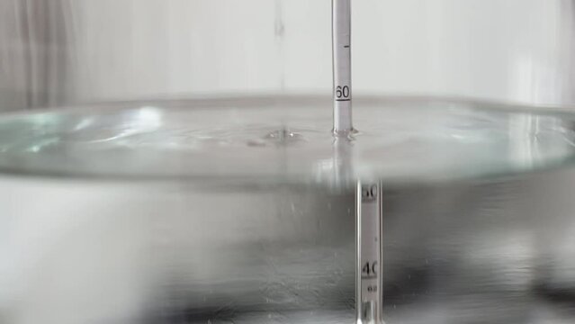 alcohol distilling process closeup - liquid distilled transparent liquid flowing in large glass jar with floating alcoholometer in it.
