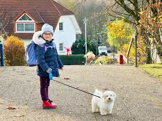 Little school girl playing with little maltese puppy outdoors after school. Happy child and family...