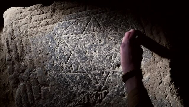 View from above, the hand of an archaeologist uses a brush to sweep away dust and clean the symbol of Israel, the six-pointed star of King David, depicted on a stone rectangular slab. land of Israel