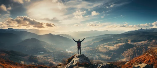 Muurstickers Young man standing on a to celebrates reaching the top of the mountain © MBRAMO