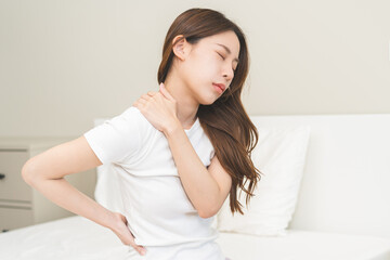 Pain body muscles stiff problem, asian young woman painful with back, neck ache from work hand holding massaging rubbing shoulder hurt, sore sitting on bed in room at home. Health care and medicine.