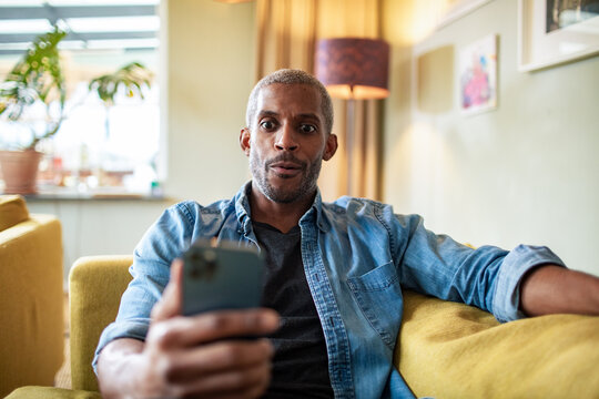 Man sitting on couch looking surprised at phone