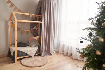 In the children's bed in the form of a house, there is a decorated Christmas tree with Christmas balls. The concept of waiting for the New Year. High quality photo