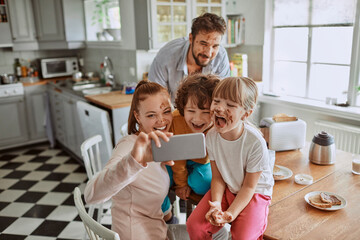 Young family taking selfie during messy breakfast in kitchen