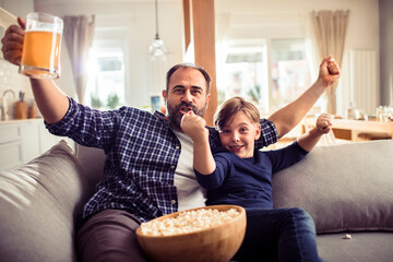 Father and son celebrating while watching sports on the couch