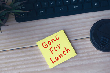 Yellow sticky note with text Gone for Lunch on wooden desk.