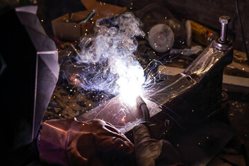 Welding old metal car part at workshop, sparks and smoke flying around, closeup detail