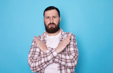 Stop gesture. Bearded man with crossed hands on blue background.
