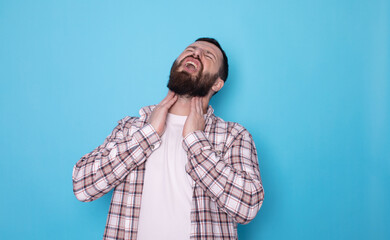 Young caucasian bearded man standing over blue background touching painful neck, sore throat for flu, cold and infection.