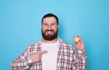 Handsome bearded man holding beard balm. Bearded man applying wax and oil to his beard on blue...