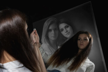 Young brunette girl is looking at her reflection in the mirror with double exposure of her portrait...