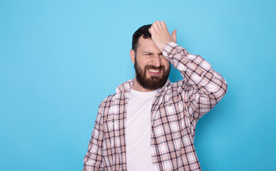 Bearded man, face palm and mistake, regret and anxiety for fail by blue background.